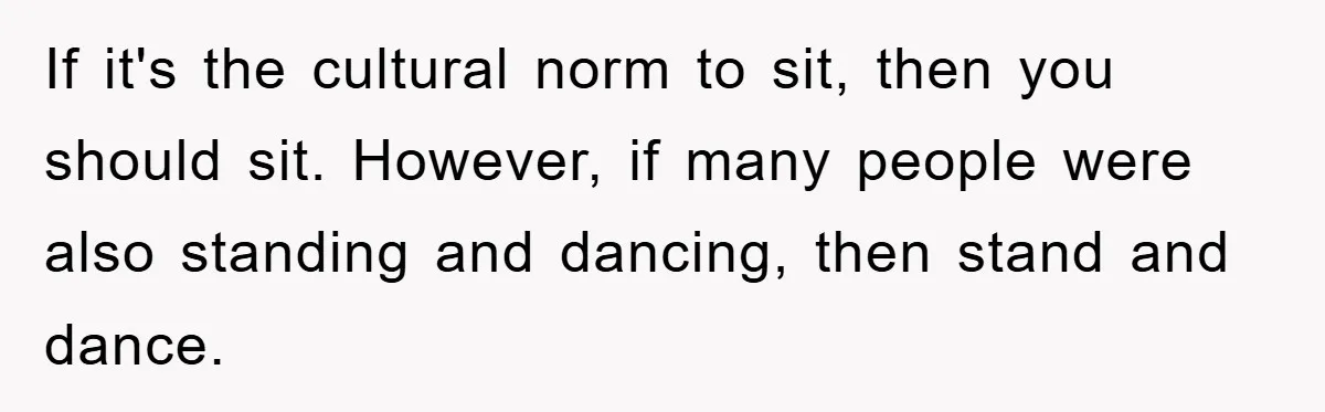 If it's the cultural norm to sit, then you should sit. However, if many people were also standing and dancing, then stand and dance.