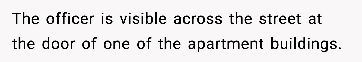 The officer is visible across the street at the door of one of the apartment buildings.