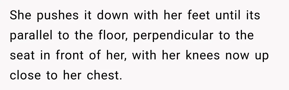 She pushes it down with her feet until its parallel to the floor, perpendicular to the seat in front of her, with her knees now up close to her chest.