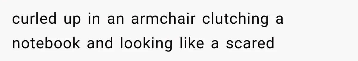 curled up in an armchair clutching a notebook and looking like a scared